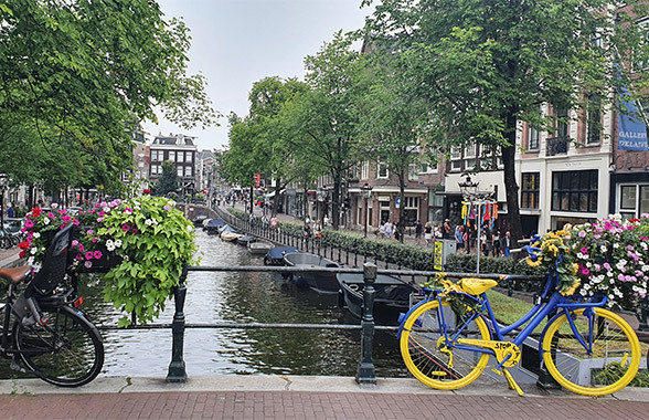 Vista di un canale adornato di fiori ad Amsterdam, con biciclette appoggiate alla ringhiera del ponte