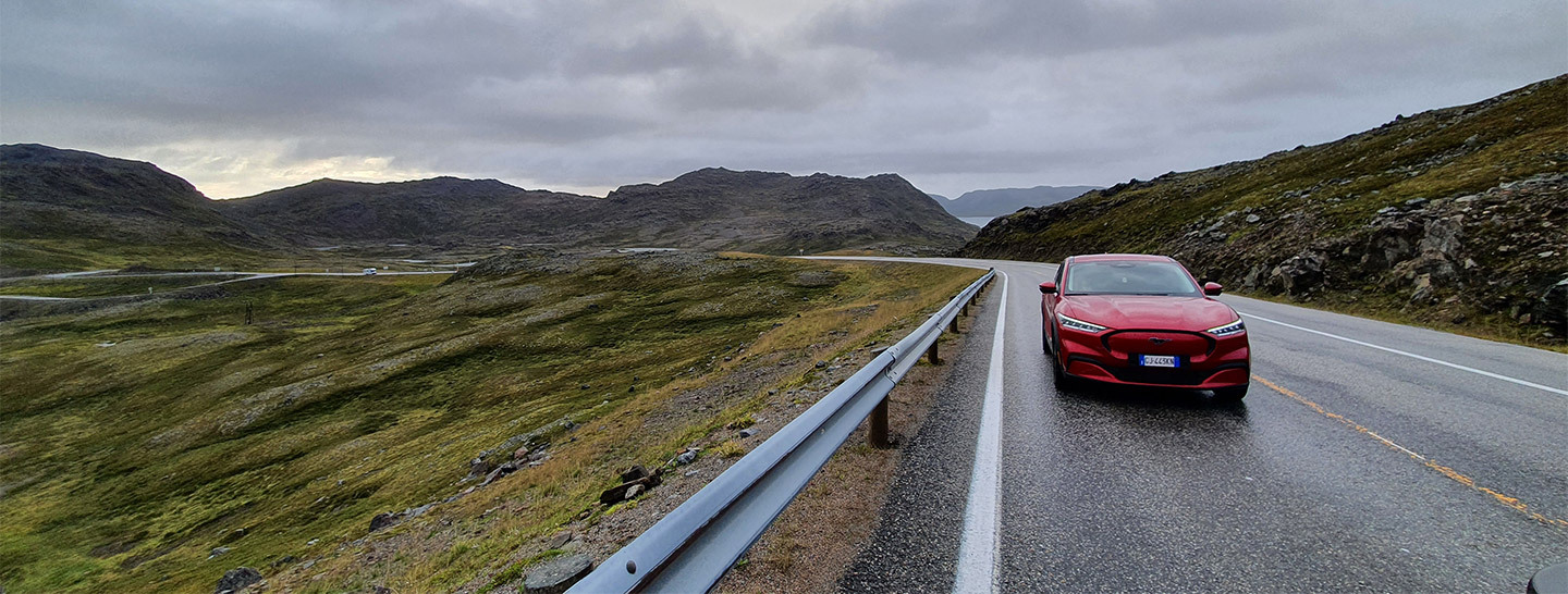 Auto elettrica Ford Mustang Mach-e rossa che viaggia su una strada del nord Europa